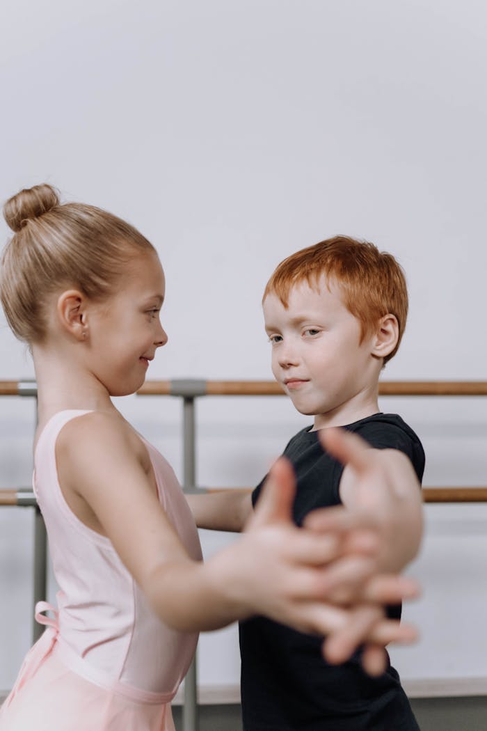 A young boy and girl dance ballet together in a studio, sharing a joyful moment.