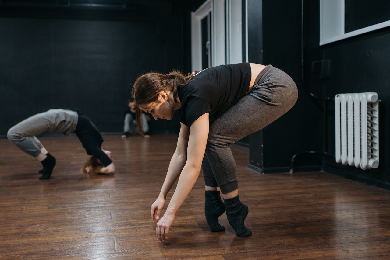 Women practicing contemporary dance movements in a studio with wooden floor.